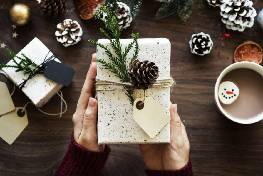 białe pudełko prezentowe z kokardką w rękach na świątecznym stole