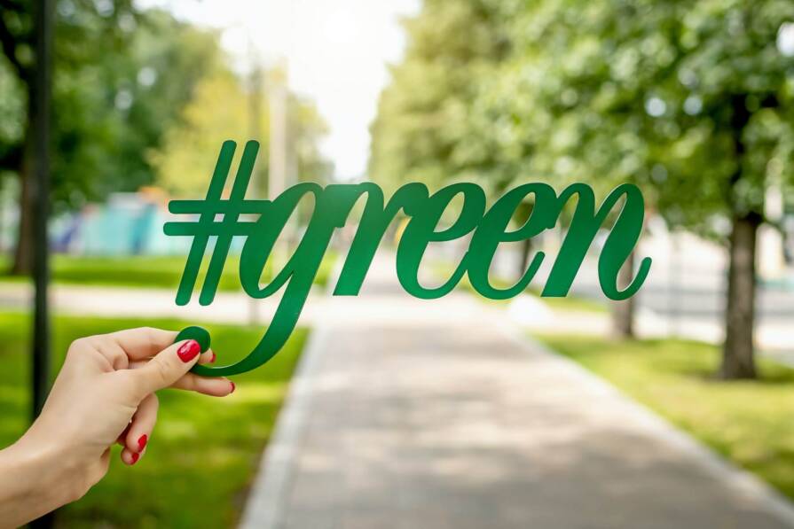 napis green w ręku z czerwonymi paznokciami na tle parku